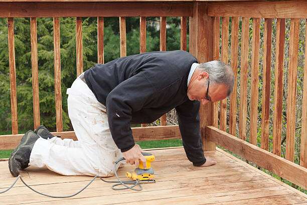 A man is sanding an outdoor deck.